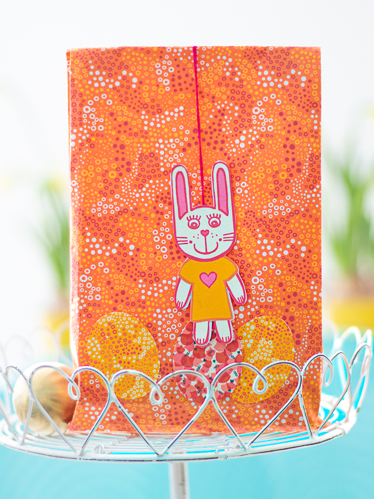 Geschenktüte aus bunten Papier für Ostern dekoriert mit einem Hasenanhänger aus Papier und Papierostereiern
